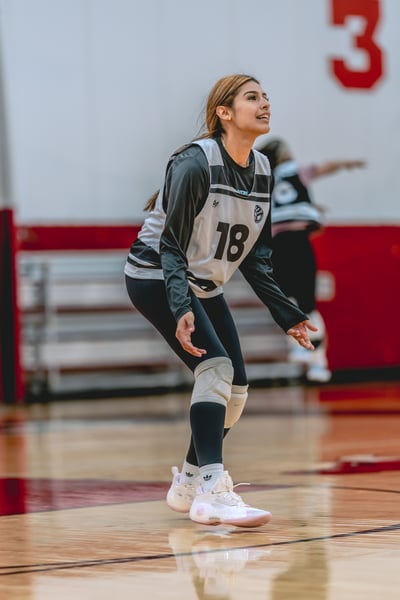 A player in a gray and white uniform crouches on a wooden court.