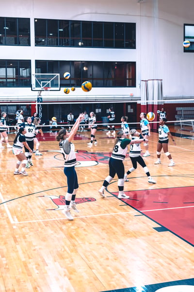 A player in white and black reaches overhead for the ball while other players in white and black and blue and white stand ready.