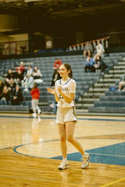 A player in white shorts and a white top claps her hands on a basketball court.
