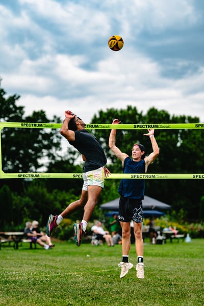 A player in black leaps to hit the ball while a player in navy jumps with arms raised.