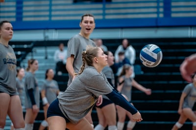 A player in a gray shirt and dark shorts reaches low for the ball.