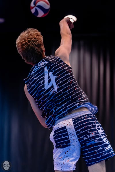 A player in a black and white patterned jersey and shorts reaches up for the ball.