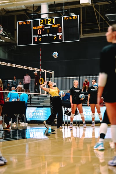 A player in yellow reaches overhead for the ball while holding another ball.