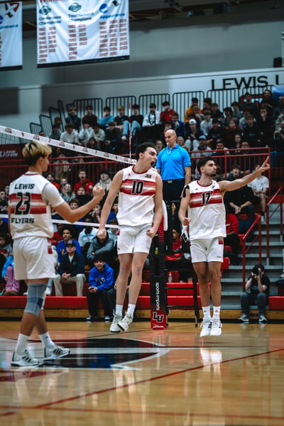 A Lewis player in white jumps with arms raised and mouth open. Another Lewis player in white points forward.