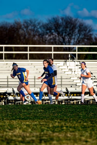 A player in blue runs with the ball, while players in white and blue run nearby.