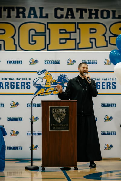 A man in black stands at a podium speaking into a microphone.