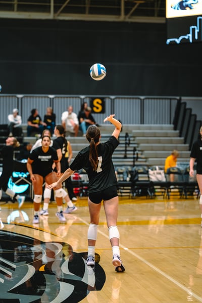 A player in black reaches overhead for the ball while other players in black watch.