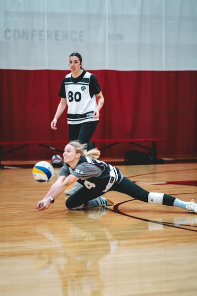 A player in black and white extends low for the ball while another player in black and white stands behind.