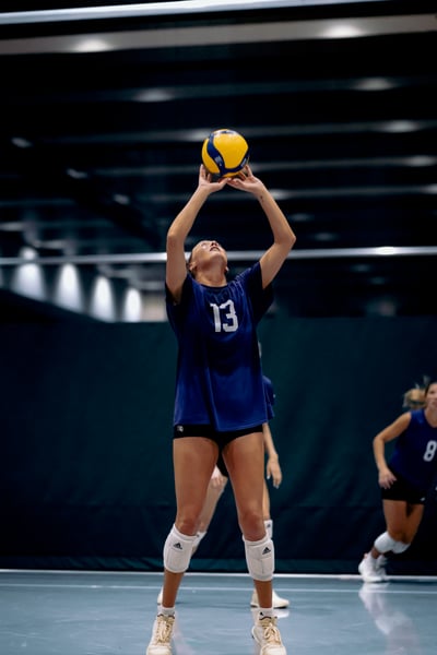 A player in a blue shirt reaches overhead for the ball.