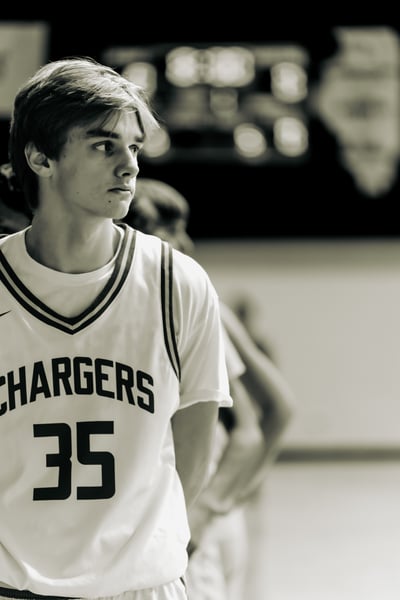 A player in white stands with arms behind their back, looking to the side.
