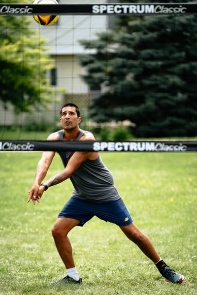 A player in a gray tank top and blue shorts crouches with arms extended toward the ball.