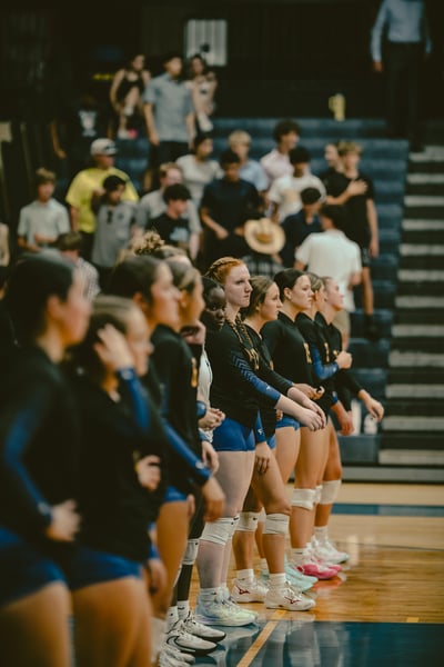 Players in black tops and blue shorts stand in a line on a wooden court.