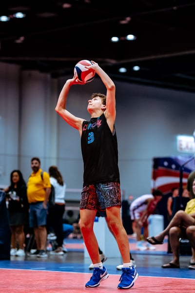 A player in a black top and colorful shorts reaches overhead for the ball.