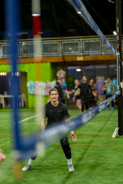 A player in black crouches with one hand extended forward on a green court.
