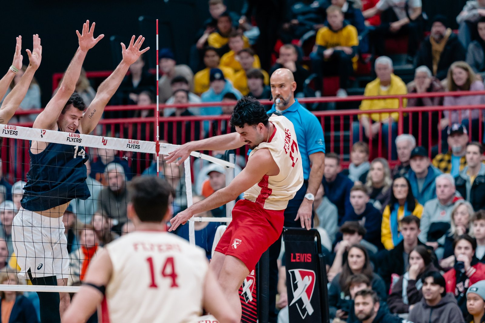 Volleyball players in navy and red uniforms compete at the net during a Lewis vs Pepperdine game.