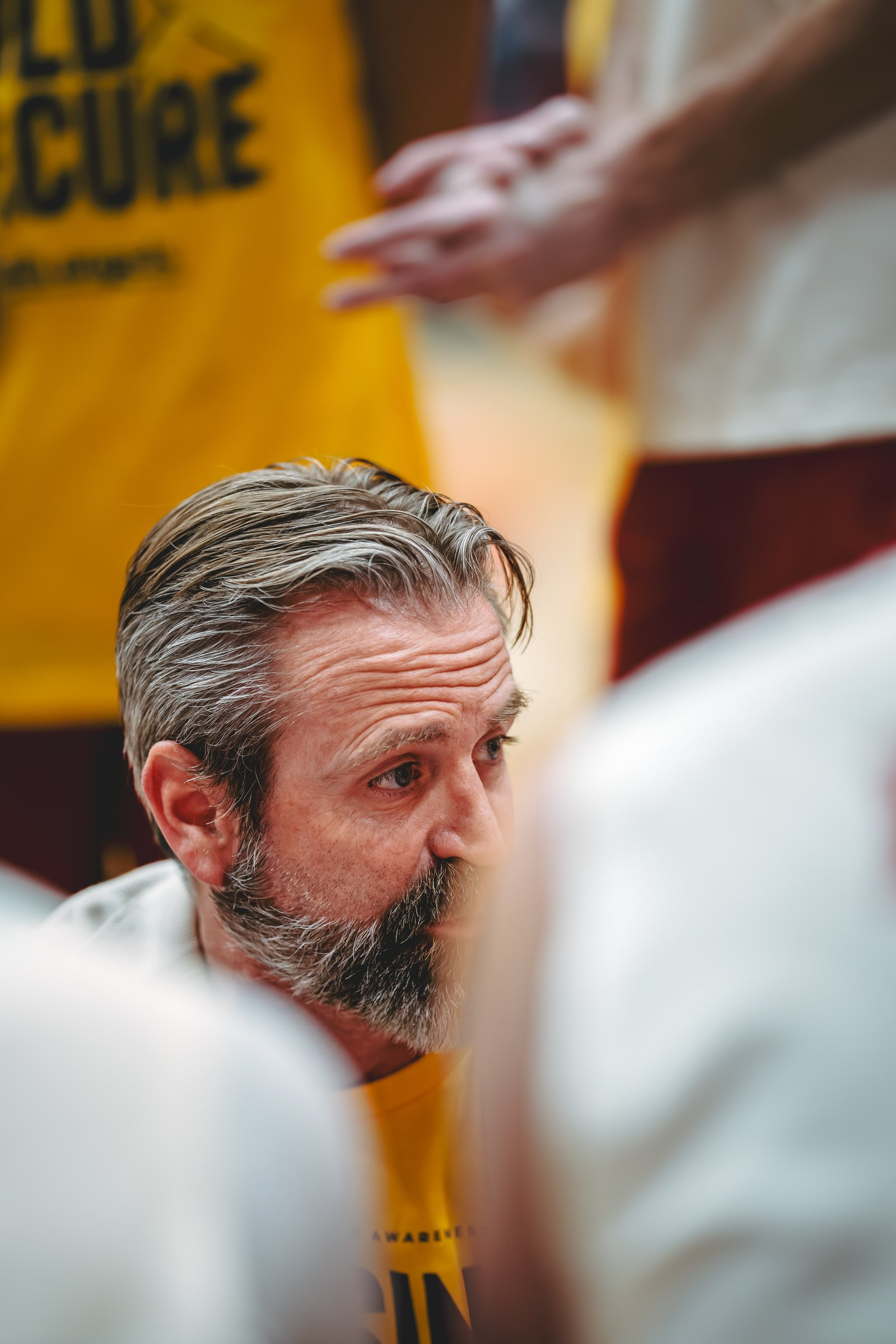 A coach with a beard looks intently at his team during a huddle.