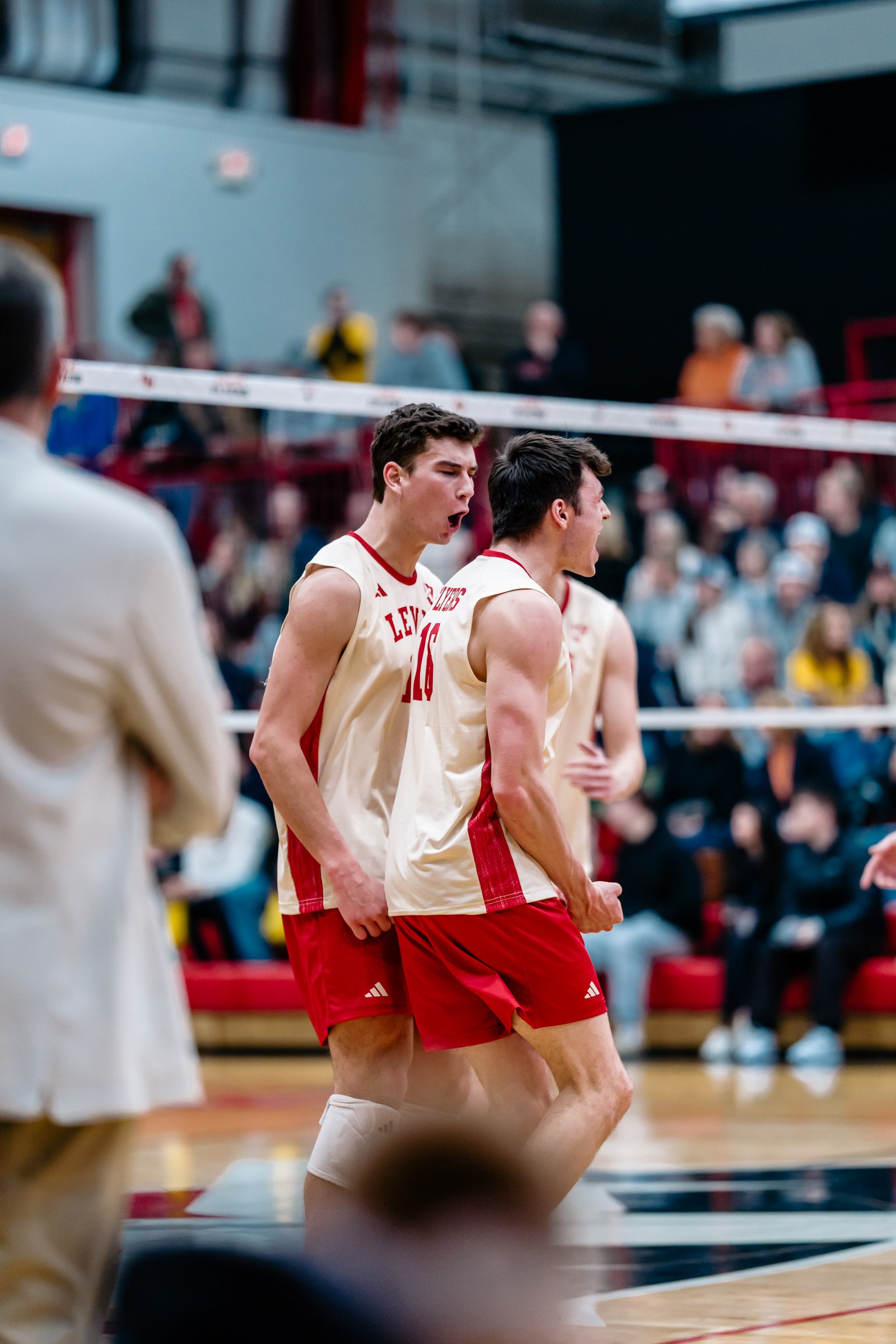 Two Lewis University players in red and cream uniforms celebrate during a volleyball match.