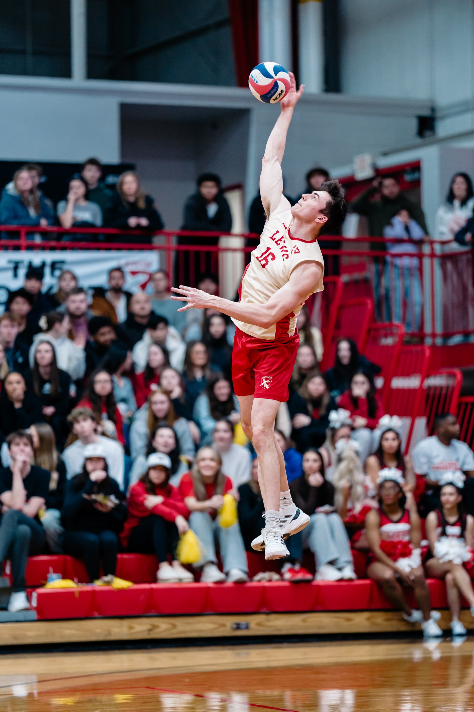 A volleyball player in a red and gold uniform serves the ball during a game.