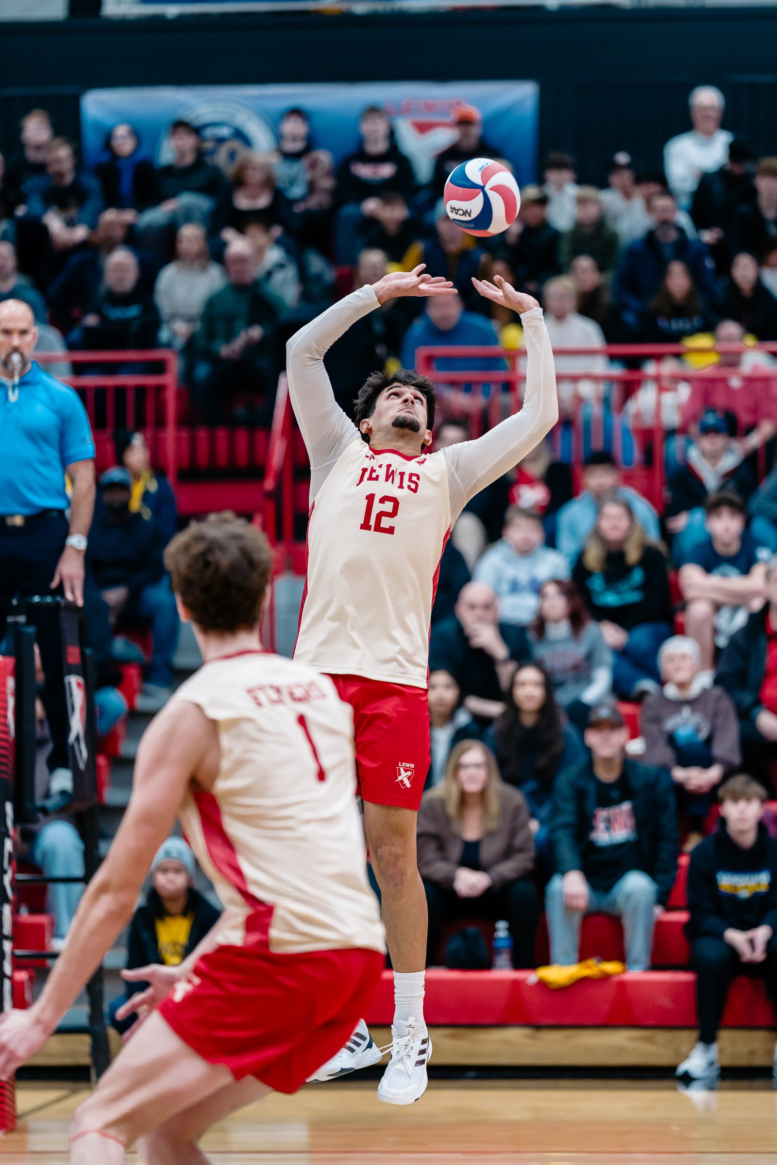 A volleyball player in a white and red jersey with number 12 sets the ball during a game.