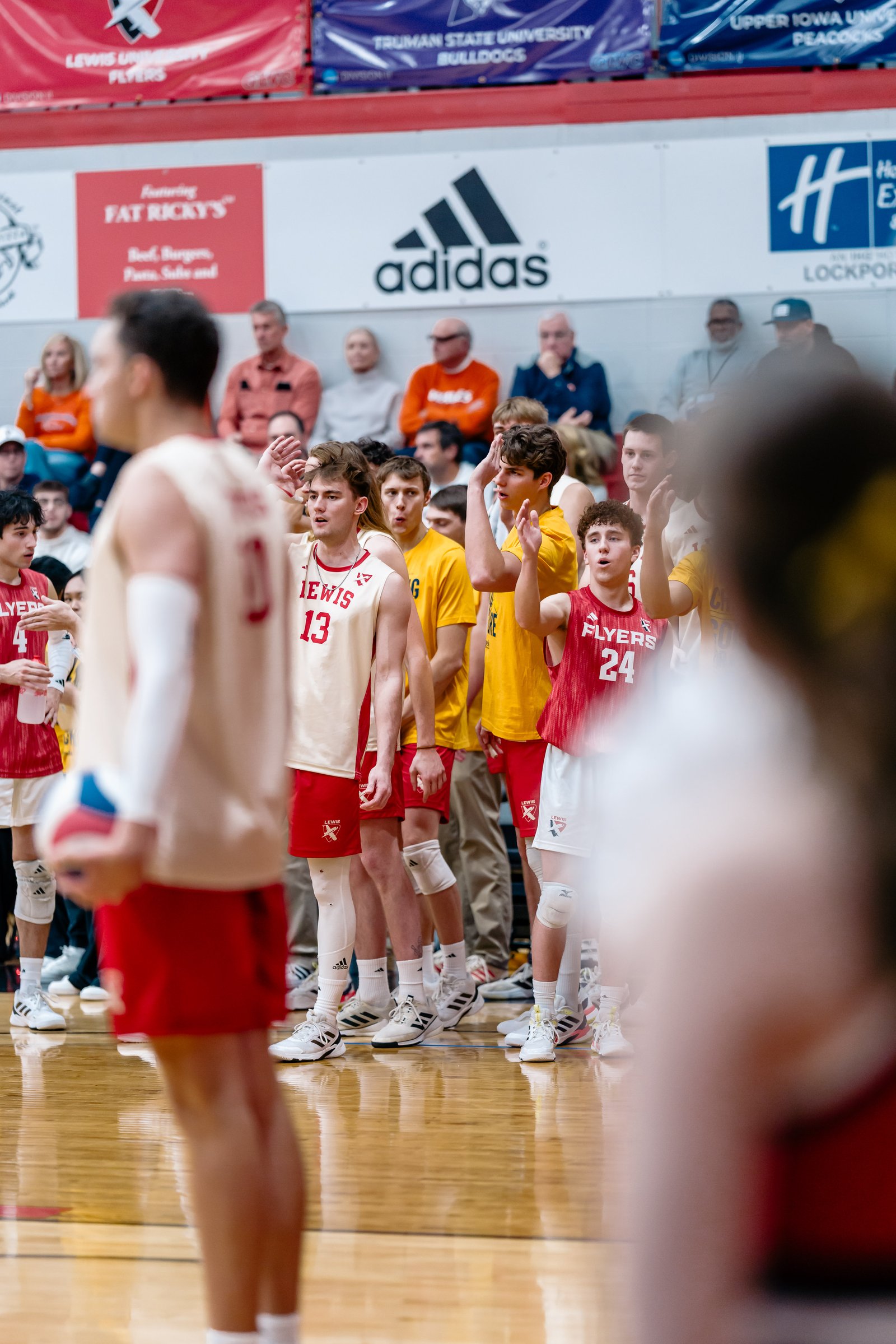 Volleyball players in red and yellow jerseys stand on the court during a game.