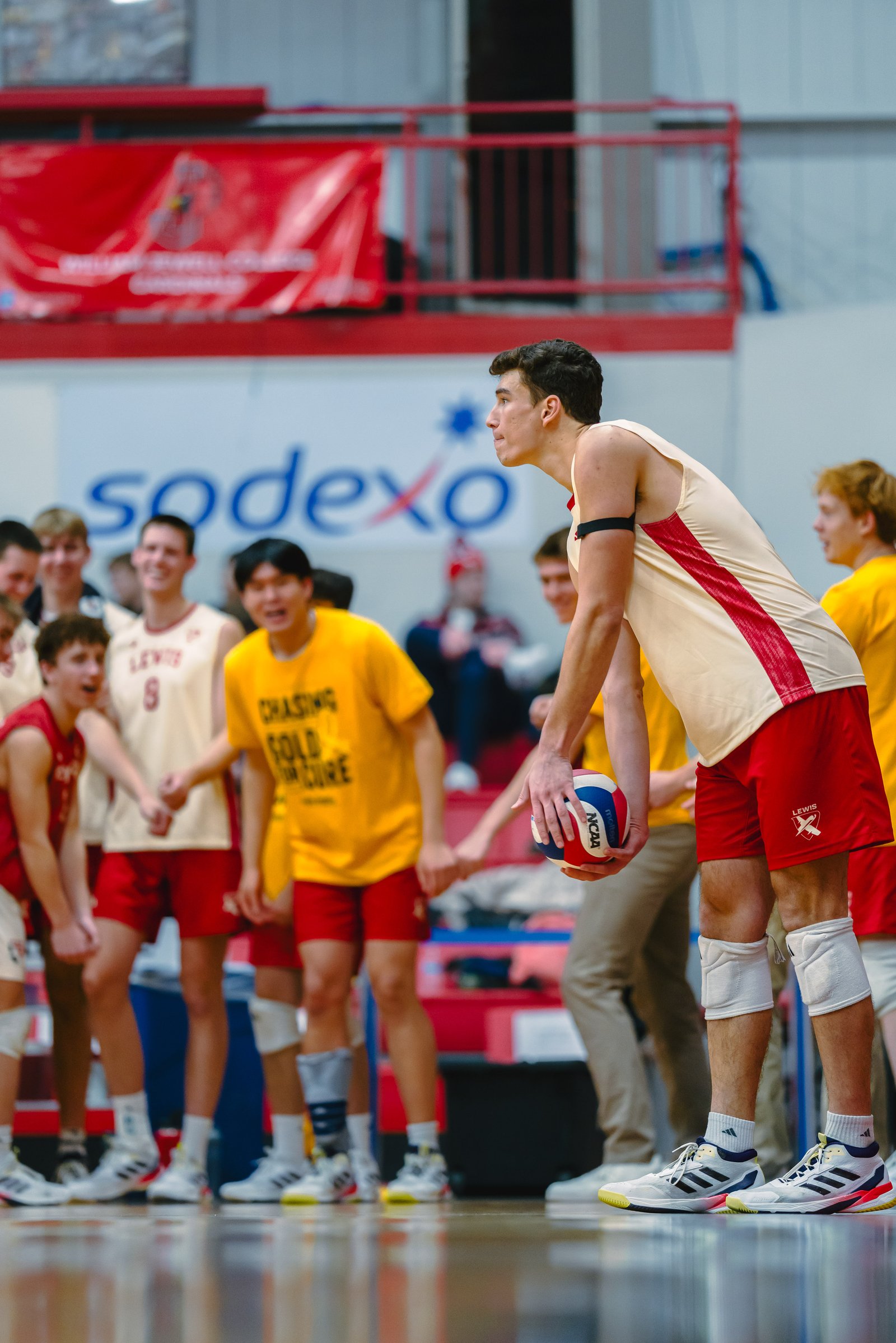 Volleyball players in red and yellow uniforms on the court, one holding a ball.