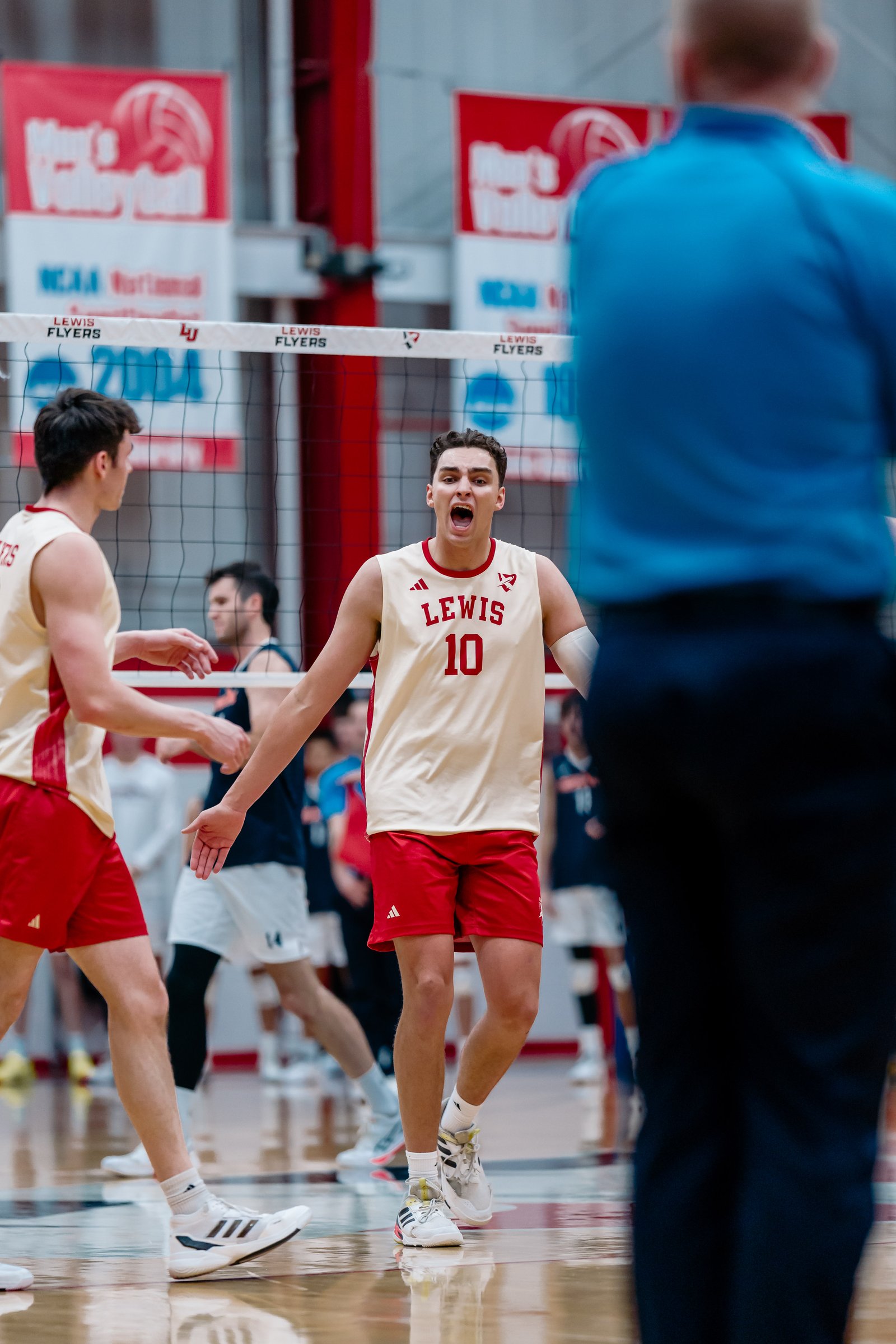 A Lewis Flyers volleyball player in a cream and red uniform with number 10 yells on the court.