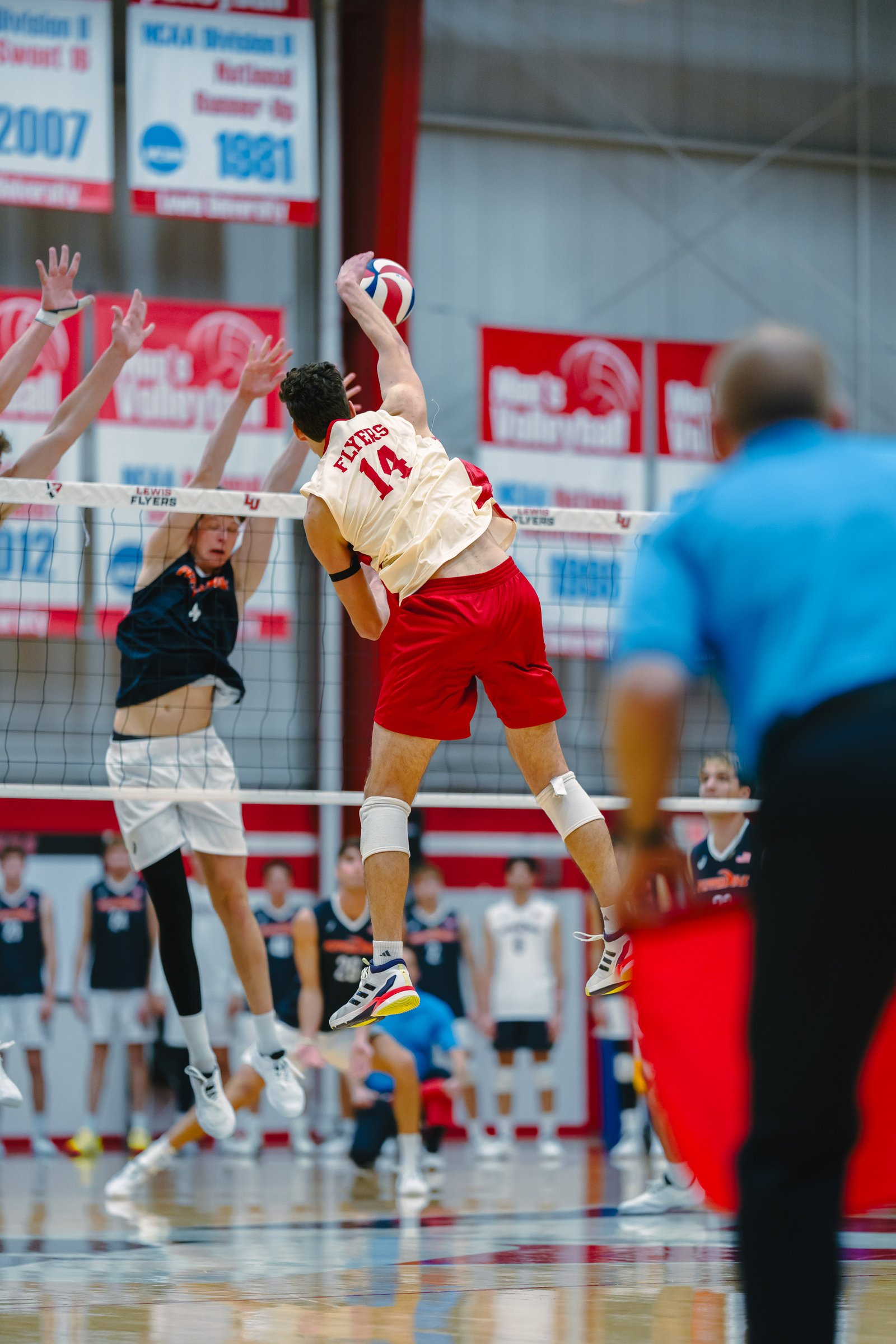 Volleyball player in red shorts spikes the ball over the net during a game.