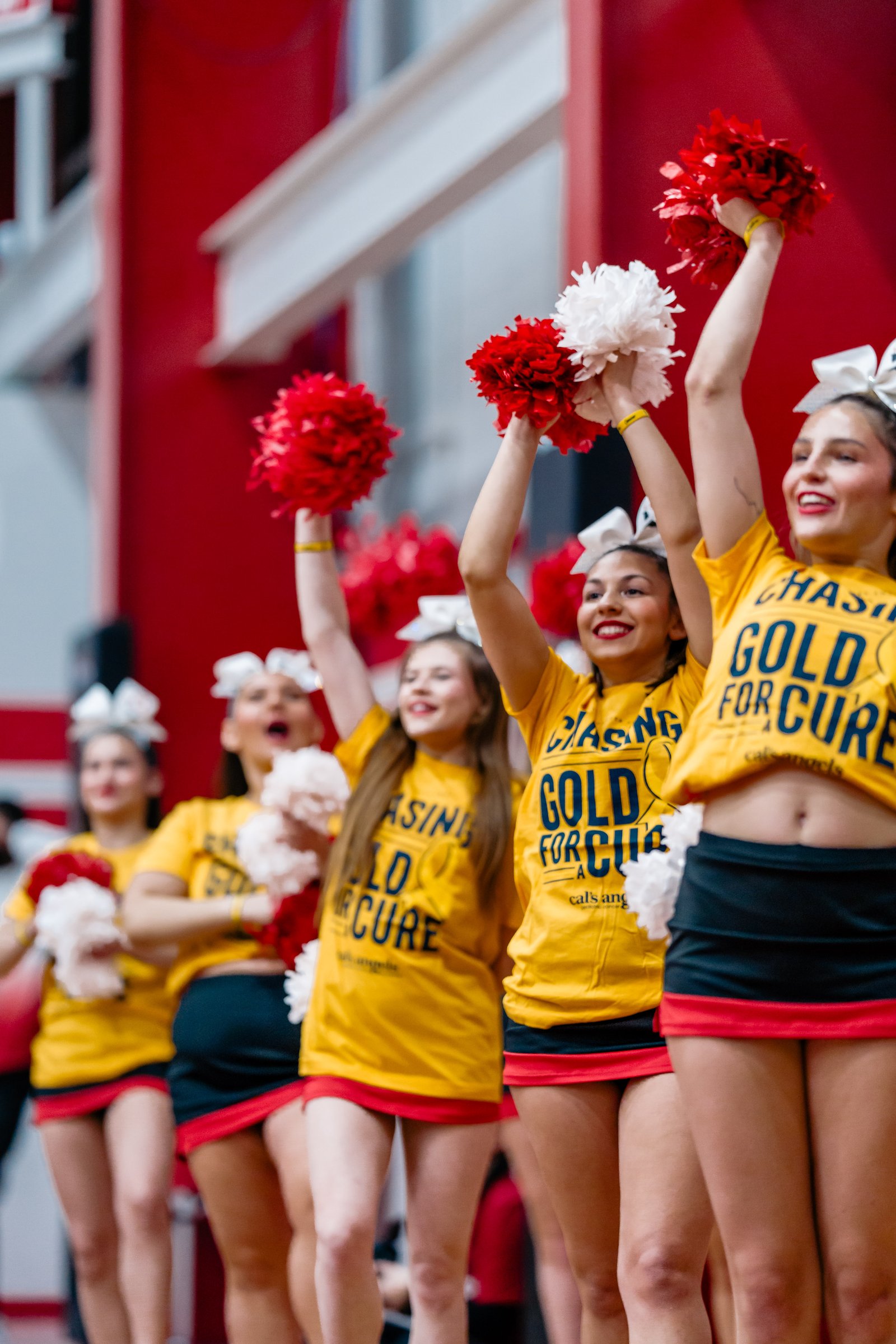 Cheerleaders in yellow shirts and black skirts with red trim cheer with red and white pom-poms.