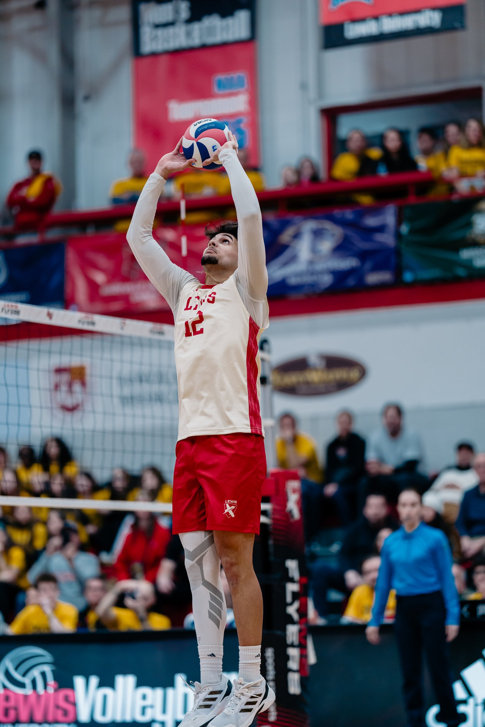 A volleyball player in a white and red uniform with number 12 prepares to serve the ball.