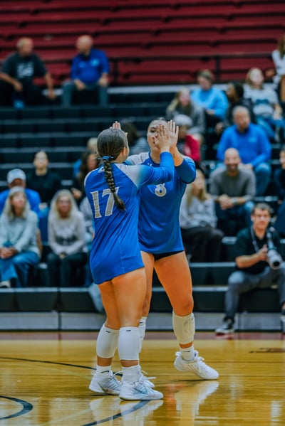 Two players in blue uniforms high five on a wooden court.