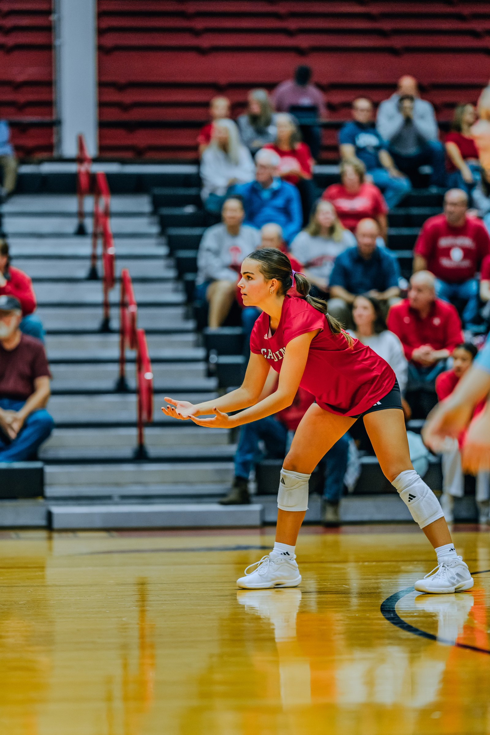 A player in a red top prepares to pass the ball on the court, with spectators in the background.