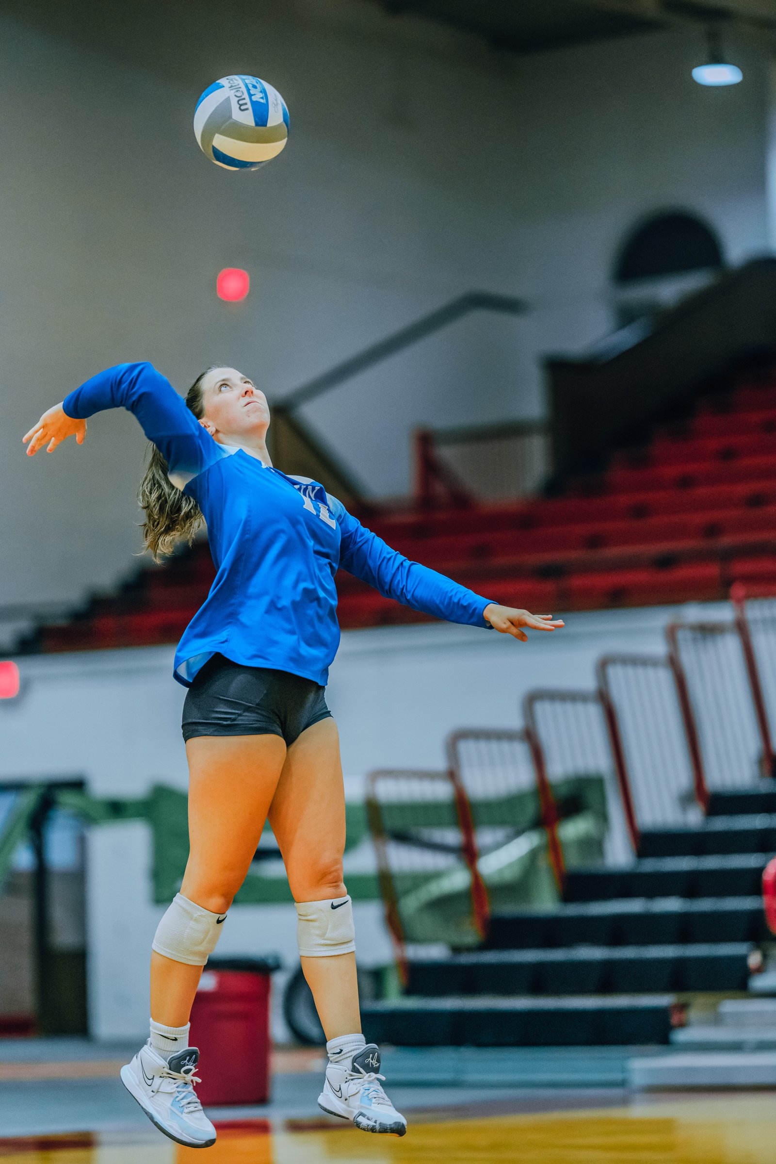 A player in a blue jersey serves the volleyball during a game.