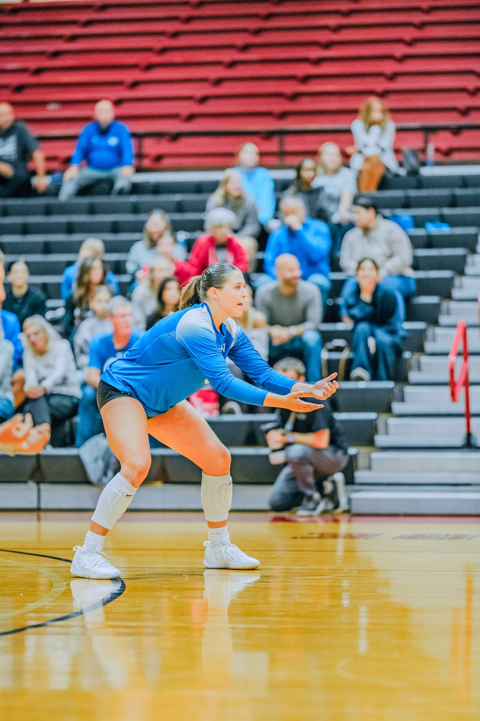 A player in a blue jersey prepares to receive the ball on the court with spectators in the background.