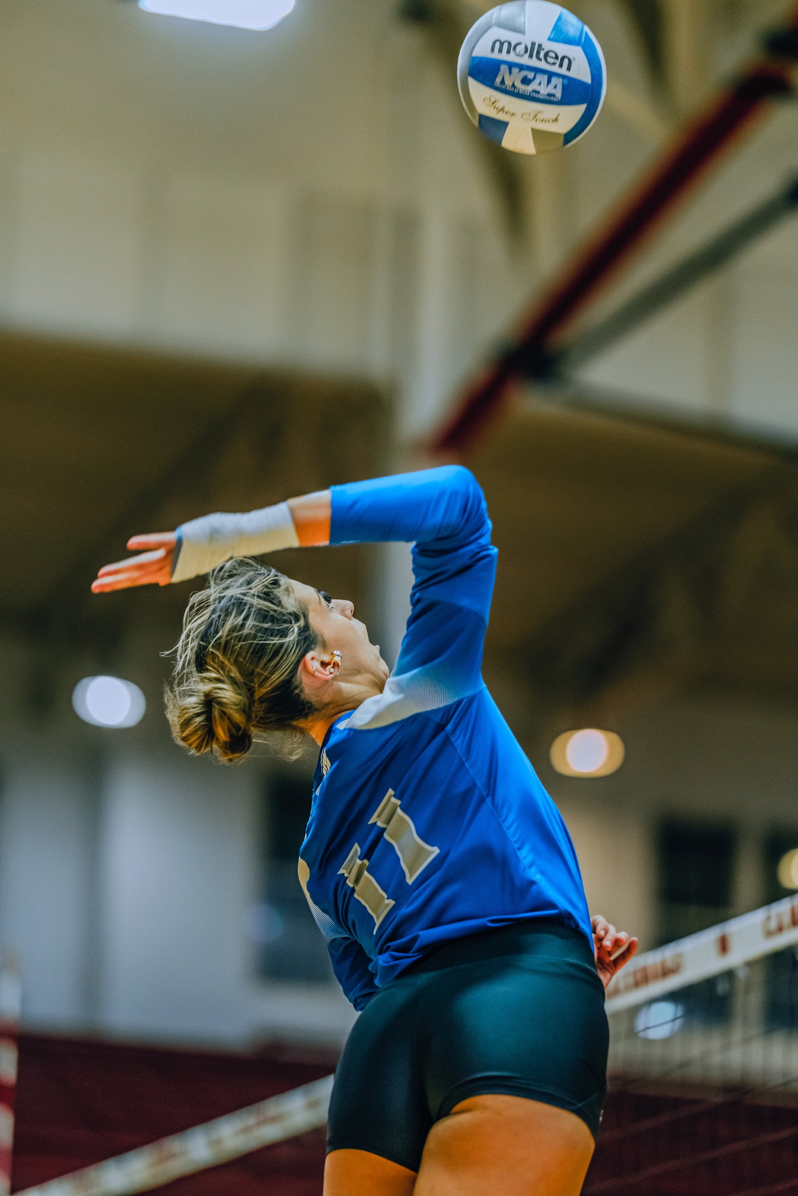 A player in a blue jersey with number 11 serves the volleyball during a game.