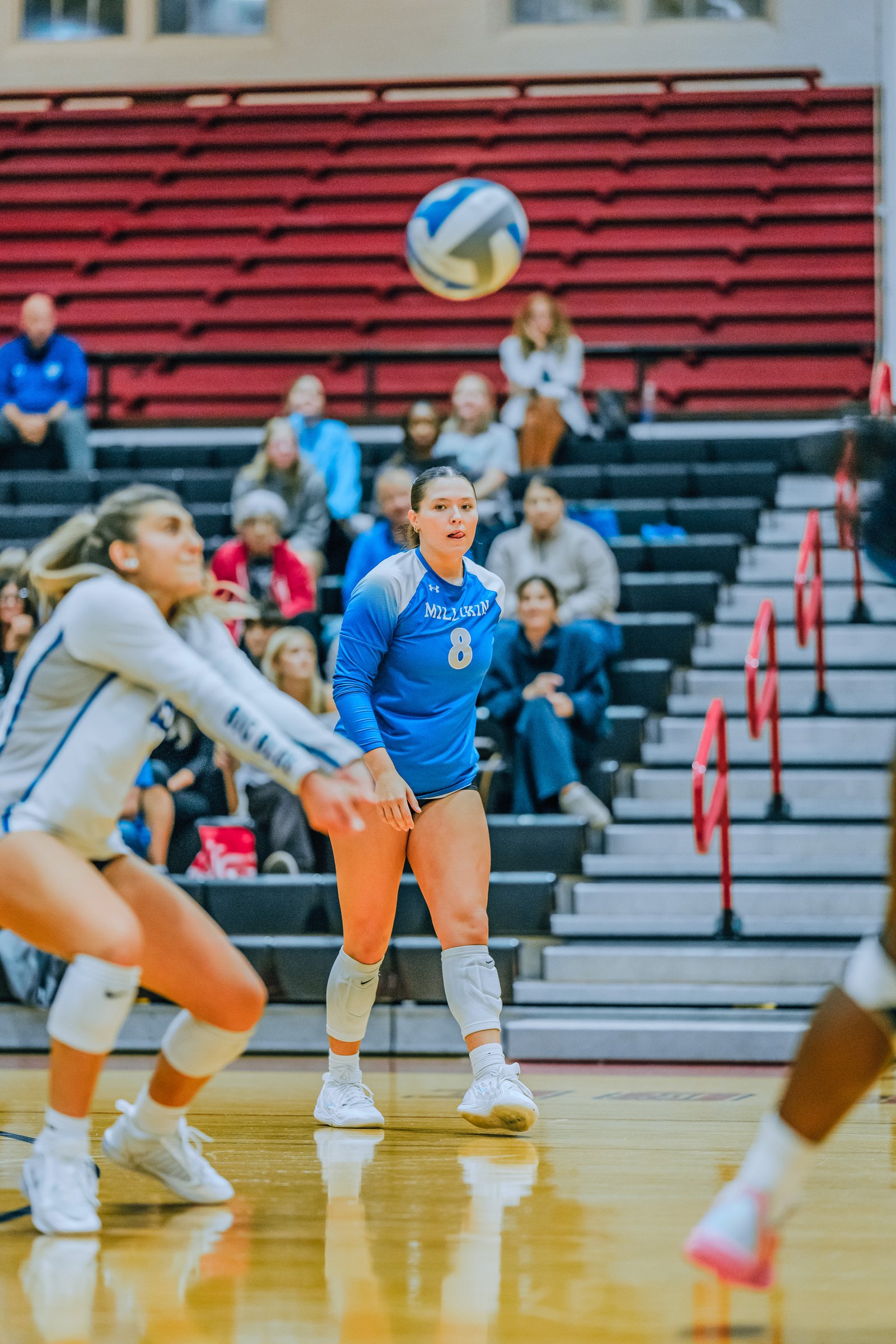 A player in blue with jersey number 8 prepares to receive a volleyball, with a player in white in the foreground.