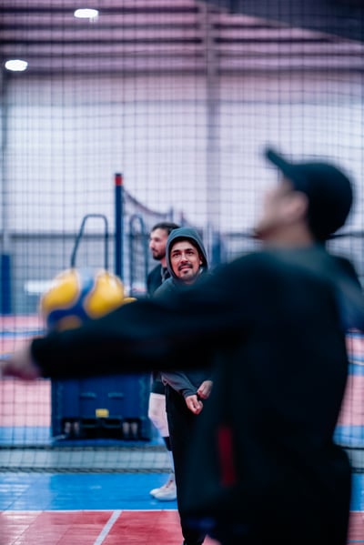 A player in black reaches for a yellow and blue ball while two players in gray watch.
