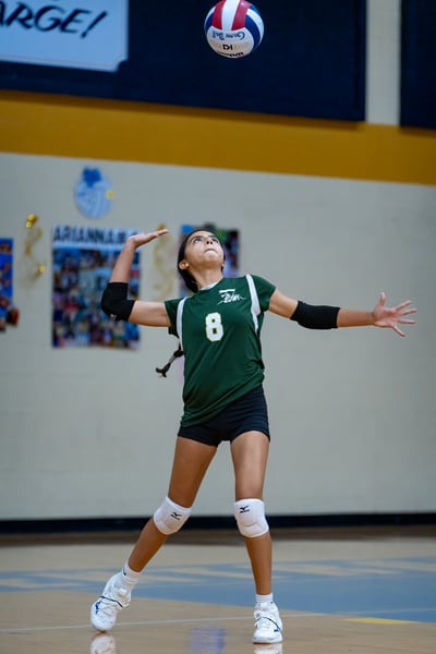 A player in a green top reaches overhead for the ball.
