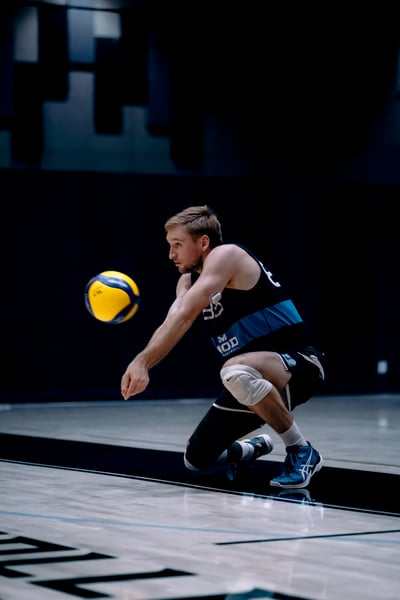 A player in black shorts and a black tank top crouches to hit the ball.