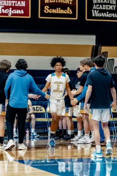 A player in white and gold stands with arms outstretched to slap hands with teammates.