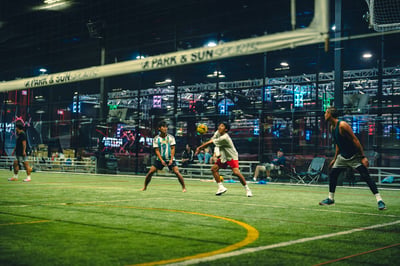 A player in white and blue reaches for the ball while a player in gray and red bends forward.