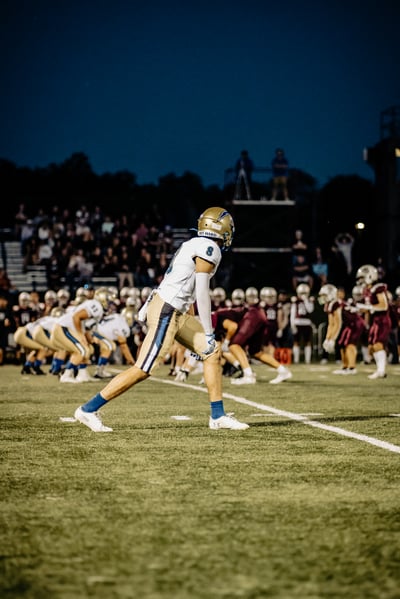 A player in white and gold crouches on a football field.