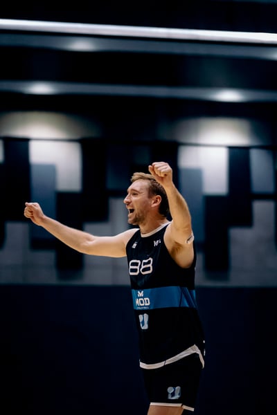 A player in a black jersey with blue trim raises his fists and shouts.