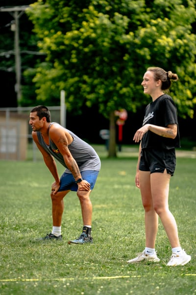 A player in gray bends with hands on knees while a player in black stands with arms open.