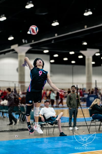 A player in a black and pink jersey jumps with arms extended toward the ball.