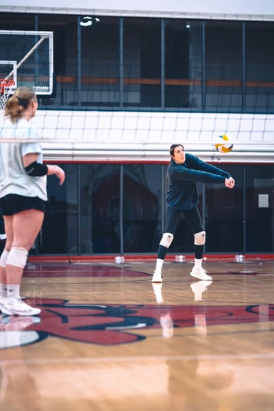 A player in dark clothing extends their arms to hit a volleyball over the net.