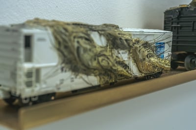 A model train car with a textured covering and a blue logo.