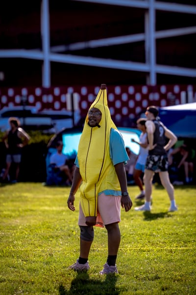 A person in a yellow banana costume stands with hands open on a grassy field.