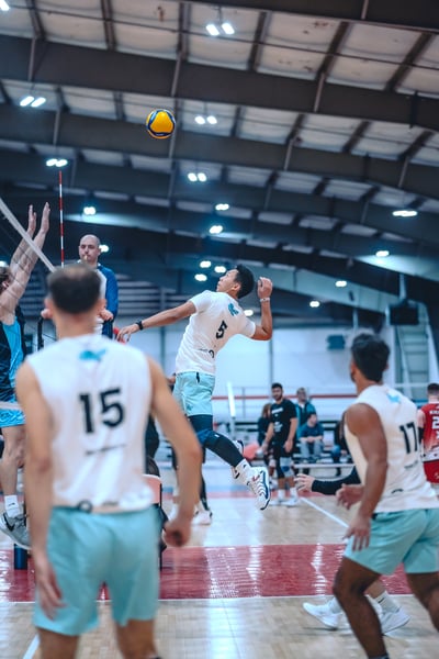 A player in white jumps and swings at the ball in a gym.