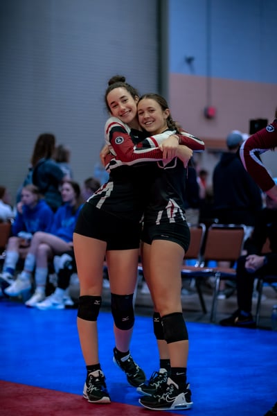 Two players in black and red uniforms hug each other on a blue court.