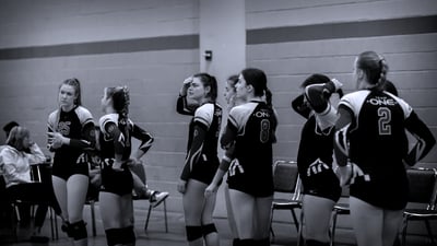 Players in black and white uniforms stand with hands on hips and one player touches her forehead.